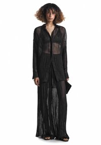 Camicia lunga nera in chiffon plissettato e pantaloni abbinati. Tessuto leggero con una texture leggermente trasparente. Chiusura con bottoni sul davanti, maniche lunghe.