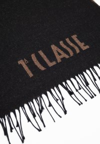 Sciarpa di lana nera con testo "1ª CLASSE" in marrone chiaro; rifinita con bordi frangiati per texture e dettaglio.