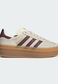 Μπεζ σουέτ αθλητικό παπούτσι Adidas Gazelle με μαρόν ρίγες, σόλα πλατφόρμας από καουτσούκ και λογότυπο Adidas ανάγλυφο στη σόλα.