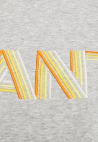 Tejido gris con texto bordado de colores brillantes. Las letras presentan hilo amarillo, naranja y blanco en un diseño a rayas con diferentes anchos.
