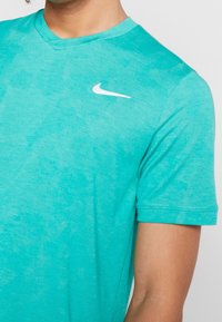 Person i en turkos Nike V-hals t-shirt med kort ärm och en vit Nike swoosh-logotyp på vänster bröst.