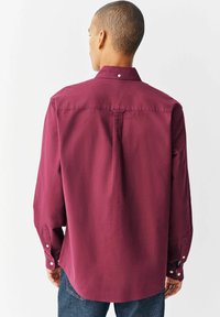 Bordeaux overhemd met lange mouwen en een button-down kraag, voorzien van een rugplooibroek en knoopmanchetten, gemaakt van gladde stof.