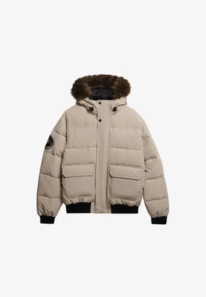 Beige puffer jacket with a fur-trimmed hood, front zip, and snap closures. Features two large front pockets and ribbed cuffs and hem.