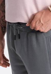 Grå bomulds sweatpants med elastisk talje, justerbar snor og sidelommer. Glat overflade, enkel design.