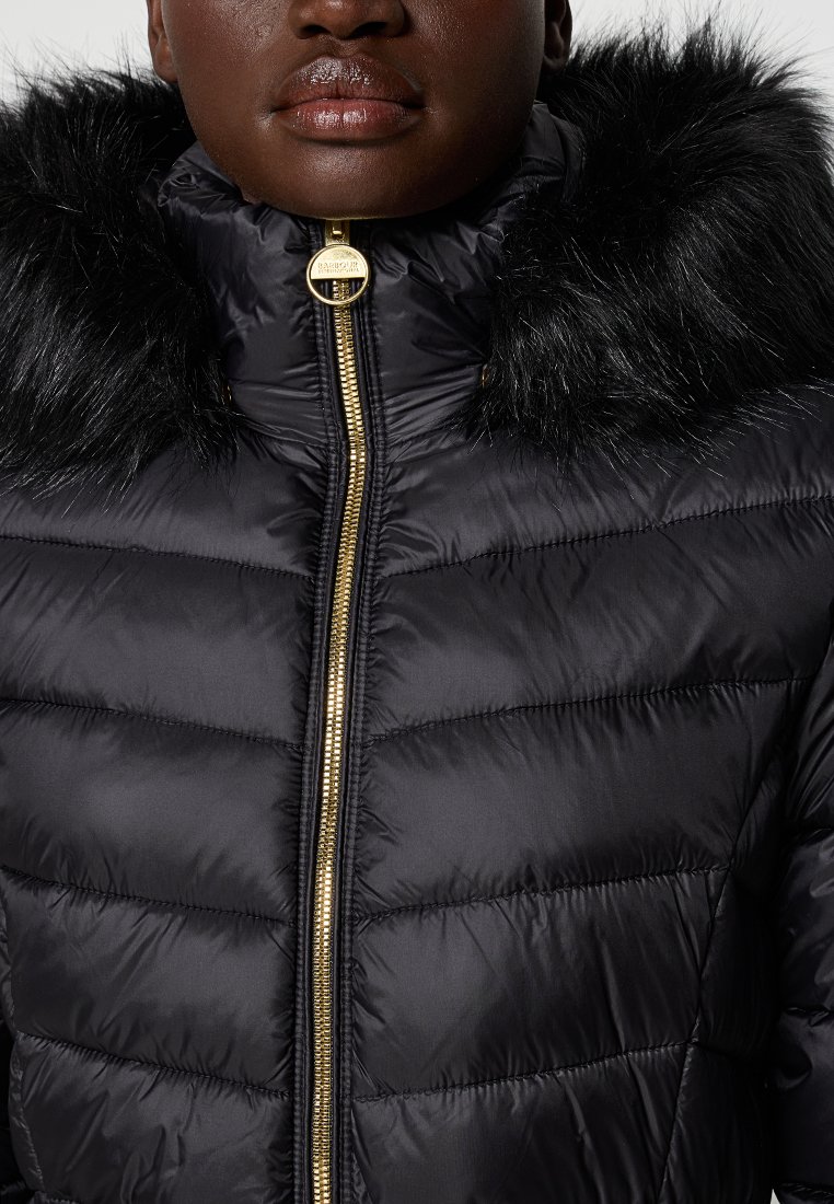 Schwarze gepolsterte Jacke mit hohem Kragen, versehen mit einem Kunstfellbesatz, goldenen Reißverschluss und gestepptem Design, das ein elegantes, strukturiertes Aussehen schafft.