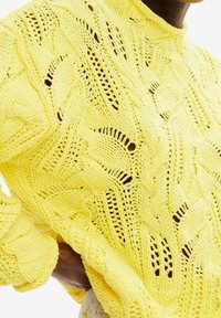 Pull-over en maille jaune vif avec un motif comprenant des torsades et des mailles ajourées, des poignets côtelés et un col montant.