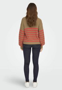 Suéter de punto en beige con rayas horizontales rojas, con un ajuste relajado y puños acanalados, combinado con jeans oscuros y zapatillas blancas.
