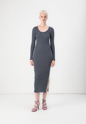 Robe longue à rayures navy et blanche, dotée d'une encolure dégagée, de fentes sur les côtés et d'une silhouette ajustée. Associée à des talons ouverts violets.