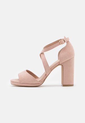 Roze suède high-heeled sandaal met een brede band over de tenen en kruislings enkelbandjes. Heeft een chunky blokhak.