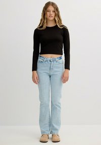 Top negro de manga larga cropped acompañado de unos pantalones rectos de mezclilla azul claro. Textura suave, diseño clásico, con un leve envejecido en las rodillas.