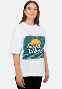 Wit katoenen T-shirt met een kleurrijke afbeelding en de tekst "Good Vibes", een zon en golven. Losse pasvorm met korte mouwen.