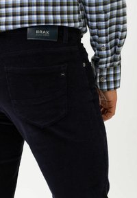 Mörkblå kordflossbyxor med ribbat mönster, utrustade med en bakficka och en märkeslapp i läder. Matchas med en rutmönstrad skjorta.