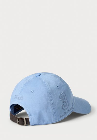 Lys blå baseballcaps laget av bomull, med buet skjerm, justerbar brun lærreim, og broderte detaljer som inkluderer "Polo" og nummeret "3."