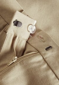 Beige fabric with a zipper closure, metal fasteners, and a clear plastic button. Textured surface with visible stitching and minor wear.