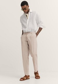 Linnenweißes Hemd, hellrosa Jogginghose mit Kordelzug, braune Sandalen. Einfaches Design, lässige Passform, leichte Textur und dezenter Farbkontrast.