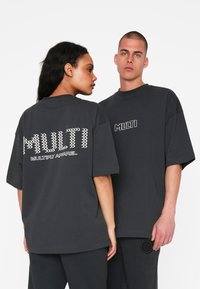 Overdimensionerede sorte bomulds T-shirts har fed hvid "MULTI" tekst på både ryggen og forsiden, med et struktureret grafisk design.