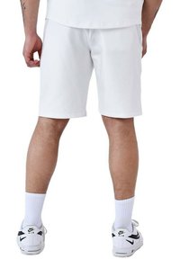 Pantalones cortos deportivos blancos, material ligero, corte hasta la rodilla, textura suave. Llevados con calcetines blancos y zapatillas Nike, con detalles en negro.