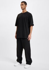 Tricou negru oversized cu mâneci scurte, asortat cu pantaloni negri cu croi lejer și adidași albi, având un design simplu și un aspect casual.
