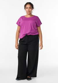 Lilla lühikeste varrukatega T-särk, millele on sobitatud laiad mustad püksid. T-särgil on ümar kaelus; pükstel on nööriga vöökoht. Mustad lamedad kingad, millel on nupukesed.