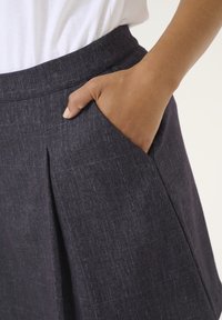 Jupe gris foncé en tissu texturé, dotée d'une taille et d'une poche latérale. Le matériau présente un motif subtil et une finition lisse.