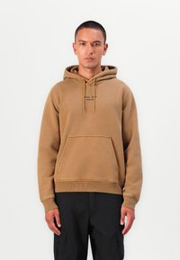 Brown hooded sweatshirt with a front pocket and drawstring. Features minimal text branding. Fabric appears soft and textured.