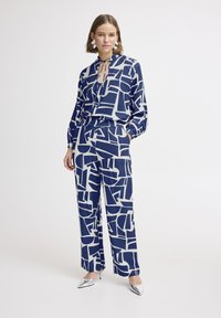 Marineblauw en crèmekleurig twee-delig ensemble met abstracte geometrische patronen, bestaande uit een blouse en brede broek met elastische taille.