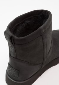 Czarny skórzany botek za kostkę z miękkim, puszystym wnętrzem. Charakteryzuje się zaokrąglonym kształtem, widocznymi szwami oraz małą pętelką z tyłu.