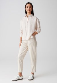 Lichtgekleurde, gestructureerde button-up shirt met lange mouwen, gecombineerd met crèmekleurige broeken en witte sneakers. De outfit heeft een relaxte pasvorm.