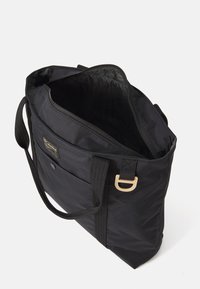 Sac fourre-tout noir en nylon durable, doté d'un zip en haut, de poches intérieures, de poignées en tissu et d'une poche à rabat à l'avant avec un patch logo.