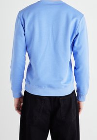 Sudadera azul claro hecha de tela suave, con cuello redondo y puños acanalados. Combinada con pantalones negros, que muestran dos bolsillos traseros.