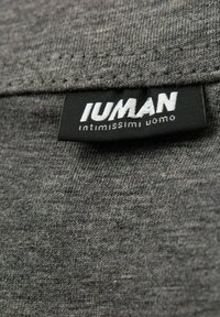 Una tela gris con una textura sutil presenta una etiqueta negra que dice "IUMAN" y "intimissimi uomo" en texto blanco cerca del borde.