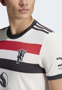 Hvit idrettsjersey med røde og svarte horisontale striper, rund halslinning og en grafisk logo på venstre brystområde.