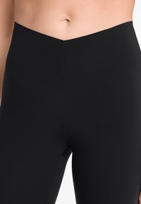 Leggings noirs taille haute avec une texture lisse, une taille en forme de V et un design ajusté qui s'étend jusqu'à mi-cuisse.