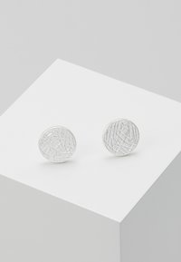 Silver circular earrings with a textured surface, featuring a pattern of intersecting lines, set on a white display.