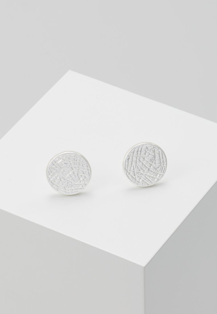 Silver circular earrings with a textured surface, featuring a pattern of intersecting lines, set on a white display.