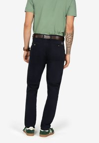 Pantaloni in cotone blu navy con vestibilità slim, tasche posteriori con bottoni e una cintura in pelle marrone. Indossati con sneakers verdi.