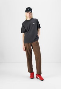 Casquette noire, t-shirt gris à manches courtes avec logo, pantalon marron ample et baskets rouges, créant une tenue décontractée avec des couleurs contrastées.