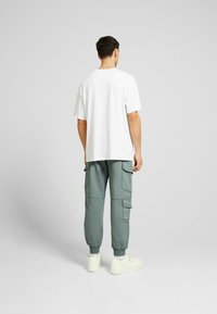 Vit kortärmad t-shirt i kombination med ljusgröna cargobyxor med flera fickor och elastiska mudd, tillsammans med off-white sneakers.