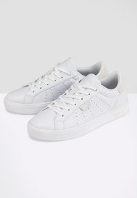Sneakers atletici bianchi realizzati in pelle liscia con dettagli perforati, lacci piatti e un accento in suede grigio sul tallone.