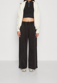 Vit zip-up hoodie med fleecfoder, svart kort topp och vida svarta byxor. Silverfärgade sneakers med distinkta detaljer.