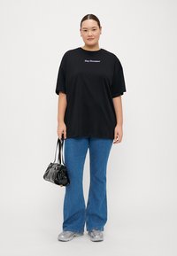 Camiseta negra de gran tamaño con el texto "Day Dreamer", combinada con jeans acampanados de color azul claro. Los accesorios incluyen un pequeño bolso negro y zapatillas grises.