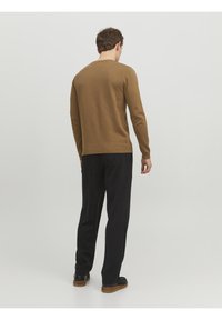 Brown knitted sweater with a round neckline, paired with black trousers. Sweater features ribbed cuffs and hem. Smooth texture.