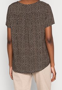 Blusa de manga corta con estampado floral marrón, escote redondo y un bajo que curvaba ligeramente en la parte trasera. Textura de tela ligera.