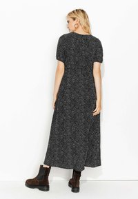 Robe longue noire avec un motif à taches blanches et des manches courtes. Portée avec des bottines en daim marron, elle a une coupe décontractée et une silhouette fluide.