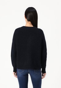 Marineblauer, strukturiertes Strickpullover mit Rundhalsausschnitt und überschnittenen Schultern. Getragen über eng anliegenden Denim-Jeans, die gerippte Bündchen zeigen.