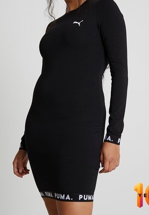 Mujer con un vestido ajustado negro de manga larga de Puma, con logotipos blancos de Puma en el pecho, los puños y el dobladillo, sobre un fondo liso.