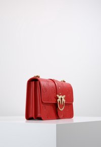 Borsa a mano in pelle rossa con motivo in rilievo, hardware dorato e fibbia circolare. Presenta una chiusura a patta e una tracolla regolabile.