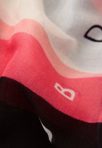 Multifarvet tørklæde med vandrette striber i koral, pink, hvid og sort samt et blødt, tekstureret stof. Bemærkelsesværdig "B"-print detalje.