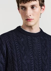 Marineblauer Strickpullover mit strukturiertem Zopfmuster und geripptem Rundhalsausschnitt. Hergestellt aus einem weichen, dicken Stoff.