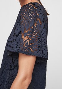 Robe en dentelle bleu marine avec un motif floral et une surface texturée, à manches courtes, laissant entrevoir la peau sous le design complexe.